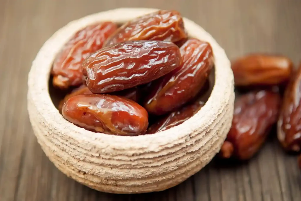 Top-down view of premium natural dates in a wooden bowl, serving as a carbohydrate-rich food source for muscle building and workout recovery.